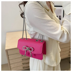 Detail of bright pink crossbody bag with silver rhinestone bow and chain strap