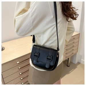 Detail view of a black faux leather saddle bag with dual strap buckles on a model