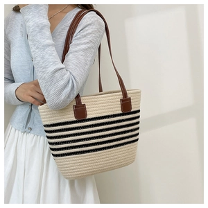 Detail of woven tote bag with black stripes and brown leather straps with white stitching
