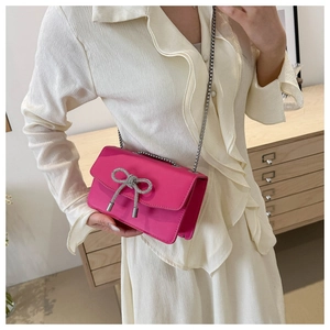 Rose red crossbody bag with crystal bow and silver chain strap shown on model