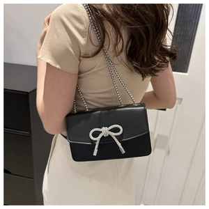 Détail d'un sac à main noir en PU avec nœud en strass étincelant et bandoulière chaîne
