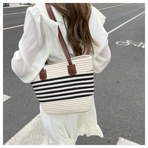 Detail of woven beach tote featuring black stripes and brown leather shoulder straps