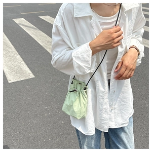 Close-up of a light green nylon drawstring bucket bag with black rope shoulder strap