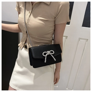 Détail d'un sac bandoulière noir avec nœud en strass argenté et bandoulière chaîne