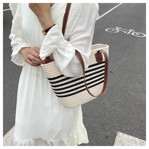 Detail of woven straw beach tote with black stripes and premium brown leather handles