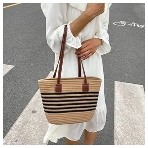 Detail of woven straw tote bag with brown leather handles and black striped pattern