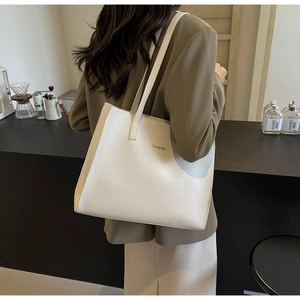 Detail of minimalist cream tote bag with gold logo and slim shoulder straps in cafe setting