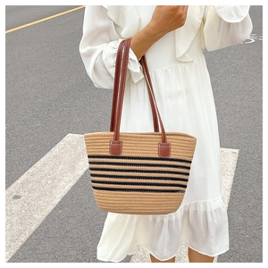 Detail of woven straw bucket bag with black stripes and brown leather shoulder straps