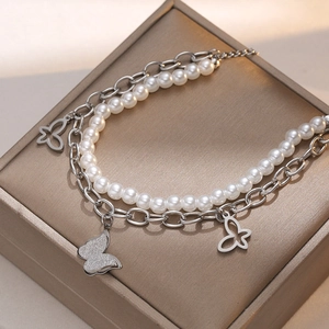 Detail of layered titanium steel bracelet with pearls and butterfly charms on jewelry box