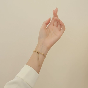 Detail of gold wheat chain bracelet with adjustable slide clasp and tassel drops on wrist