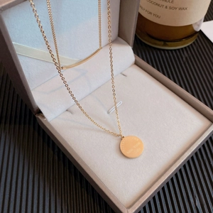 Détail d'un collier double épaisseur en titane doré avec pendentif pièce gravé en boîte