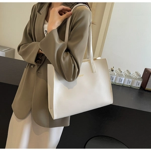 Close-up of white leather tote bag with gold lettering shown on a model's shoulder