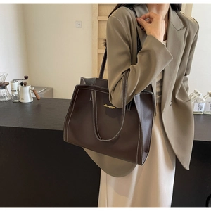 Detail view of large brown tote bag with contrast white stitching and gold logo