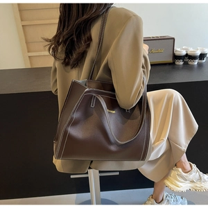 Detailed view of large dark brown tote bag with contrast stitching in urban cafe setting