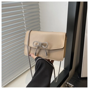 Détail du sac à rabat beige avec boucle noeud en strass et bandoulière chaîne