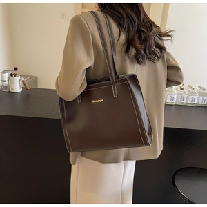 Detail of dark brown tote bag with white contrast stitching and gold logo on the side