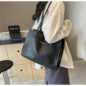 Close-up of a large black leather tote bag with white stitching and gold brand logo