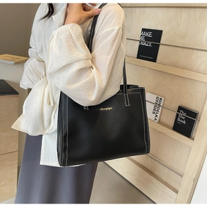 Minimalist black leather tote bag with white contrast stitching and long shoulder strap