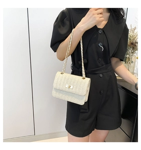 Detailed view of beige woven straw bag with gold metal clasp and chain shoulder strap
