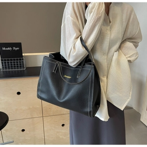 Detail view of large black tote bag featuring white contrast stitching and gold logo