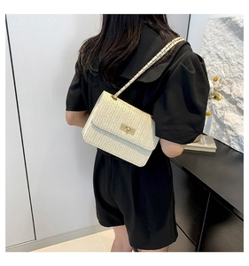 Detailed view of a beige straw crossbody bag with golden chain strap on a black outfit