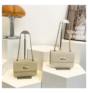 Close-up of woven straw flap bags with gold chain straps on modern geometric stands