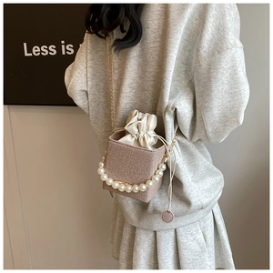 Detail of woven bucket bag featuring pearl top handle and gold metal chain strap