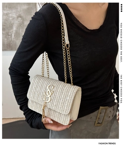 Detail of beige straw bag featuring a gold chain strap, metal logo, and fringe charm