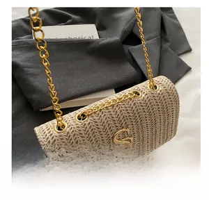 Detail of woven straw crossbody bag featuring a gold chain strap and metallic logo