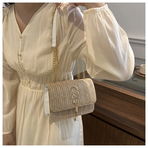 Detail of a beige straw woven bag featuring a golden S-clasp and elegant fringe tassel