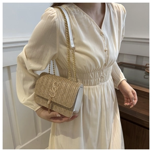 Detail of woven straw flap bag with gold S-link hardware and chain strap on cream dress