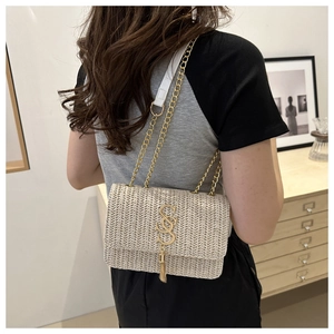Detail of woven straw crossbody bag with golden S-logo, tassel, and chain strap