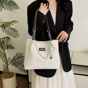 Sac fourre-tout blanc cassé avec chaîne argentée et lanières brunes porté par un mannequin