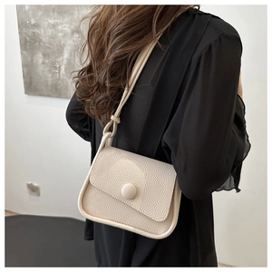 Side view of beige lychee texture saddle bag on model with minimalist round buckle