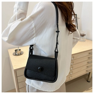 Close-up of a black lychee-textured leather saddle bag worn by a model in a cozy room