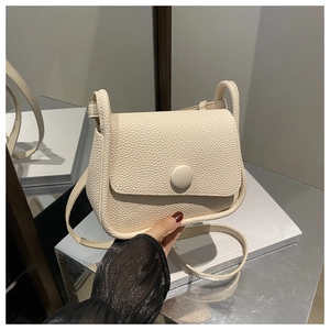 Detail of cream lychee texture saddle bag featuring a round magnetic clasp and thin strap