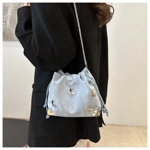 Pale blue drawstring bucket bag with butterfly studs and chain strap shown on model