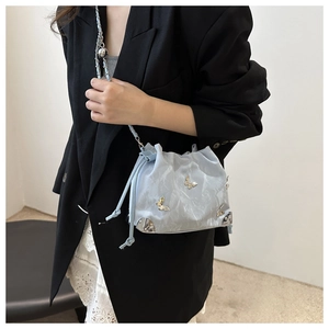 Close-up of light blue drawstring bucket bag with silver butterfly studs and chain strap