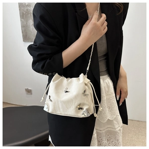 Detailed view of silver butterfly metal charms and chain strap on white drawstring bag