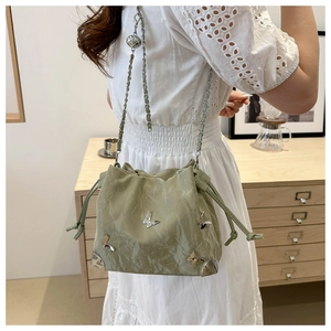 Sage green drawstring bucket bag with silver butterfly rivets and chain strap