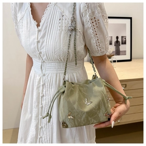 Detail of light green drawstring bucket bag with butterfly studs and metal chain strap