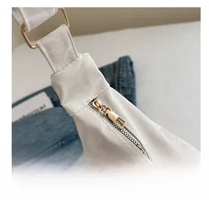 Detailed close-up of the smooth gold metal zipper and nylon fabric on a white tote bag