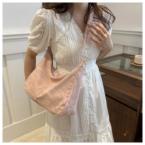 Detail of pink hobo tote bag with adjustable strap worn by model in white lace dress