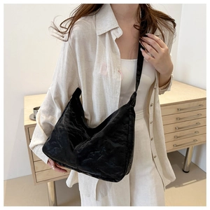 Close-up of black textured crossbody tote bag with wide strap on white linen shirt