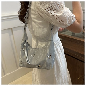 Silver shoulder bag with 3D metallic butterfly accents shown on model in a white dress