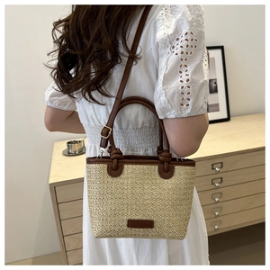 Close-up of woven straw tote bag with brown leather handles and adjustable shoulder strap