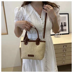 Close-up of woven straw bucket bag with brown leather trim and handles on white dress