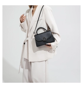 Détail d'un sac carré noir avec boucle dorée porté par un mannequin en costume beige