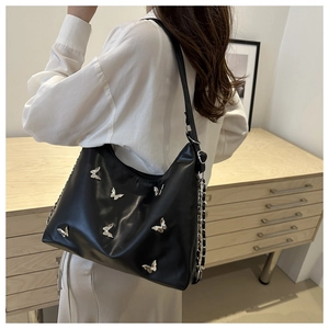 Detail of black leather tote bag with silver butterfly charms and metal chain elements