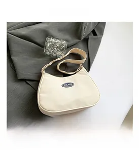 Detail shot of a minimalist cream nylon crescent bag over grey suiting fabric